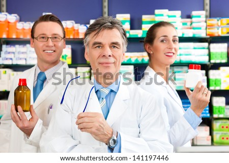 Pharmacist with his team standing in pharmacy or drugstore in front of shelves with pharmaceuticals