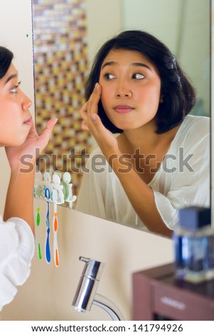 Asian woman discovering a pimple in face
