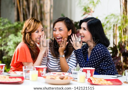 Three Indonesian friends gossip and whisper to themselves secrets in tropical environment