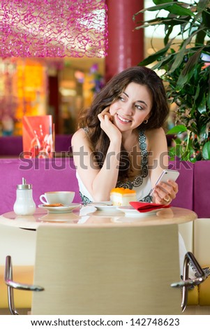 Young woman in a cafe or ice cream parlor eating a cake and using her phone, maybe she is single or waiting for someone
