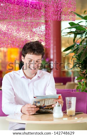 Young man in a cafe or ice cream parlor reading a magazine, maybe he is single or waiting for someone