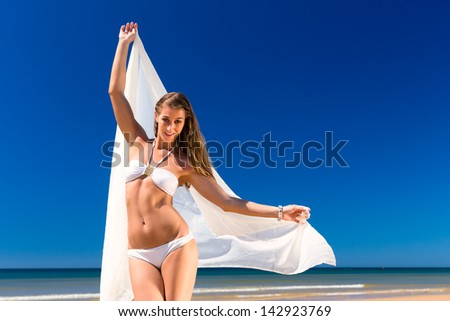 Attractive Woman in white bikini standing in the sun on beach with a white  scarf, a lot blue sky