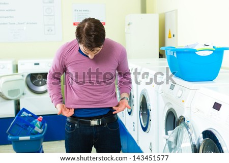 Young man in a launderette, washing his dirty laundry, in the background are washing machines, he is angry about his undersized top