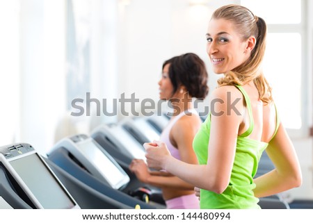 Running on treadmill in gym or fitness club - two women exercising to gain more fitness