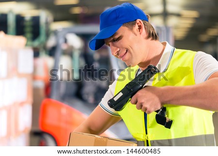 Warehouseman with protective vest and scanner, scans bar-code of package, he standing at warehouse of freight forwarding company