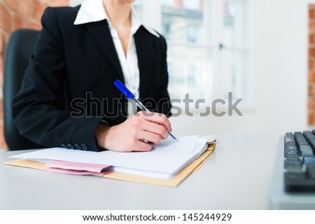 Young female lawyer or secretary working in her office and writing in a document