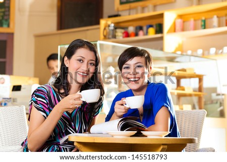 Asian female friends enjoying her leisure time in a cafe, drinking coffee or cappuccino and talking about some things
