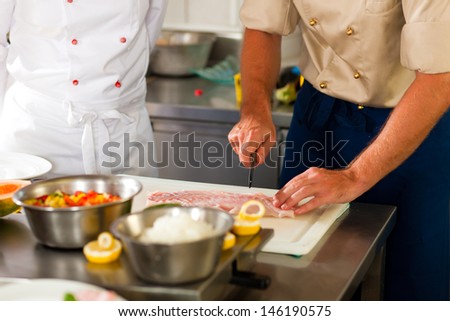 Close up of chefs in a commercial restaurant or hotel kitchen working, they are preparing an fish fillet and vegetables