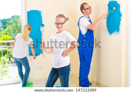 Father and his daughters or daughter with her friend are painting with paint roller a wall in blue.
