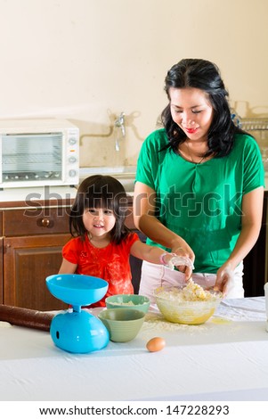 Indonesian Asian Little girl and her mother in the kitchen bake a cake together