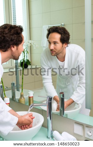 Young man in the hotel bathroom, suite, refreshing himself and washing the face at the sink