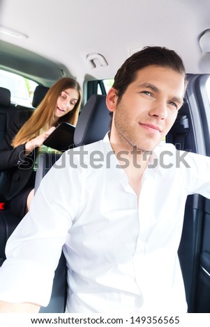 Young taxi driver driving businesswoman in taxi, she holding cup of coffee and a tablet computer
