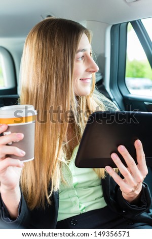 Young businesswoman traveling in taxi, she holding cup of coffee and a tablet computer