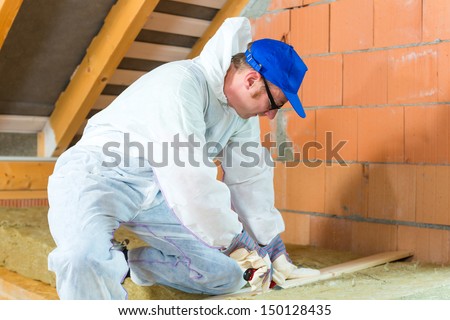 Worker in overall is cutting insulating material with gloves and knife
