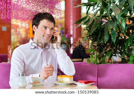 Young man in a cafe or ice cream parlor eating a cake and using his phone, maybe he is single or waiting for someone