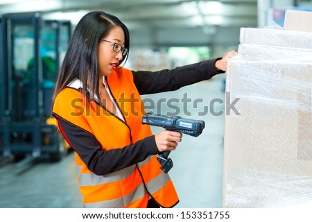Logistics - female worker or shipper with protective vest and scanner, scans bar-code of package, he standing at warehouse of freight forwarding company