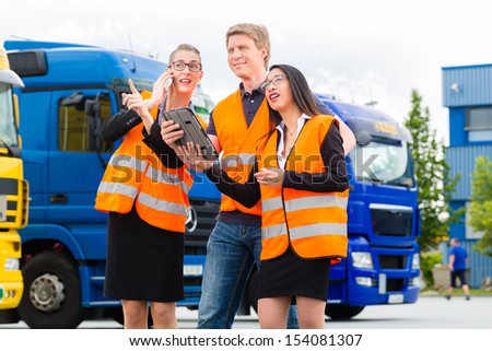 Logistics - proud driver or forwarder and colleagues with tablet computer, in front of trucks and trailers, on a transshipment point, its a good and successful team