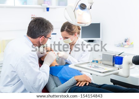 Female Patient With Dentist And Assistant In A Dental Treatment, Wearing Masks And Gloves