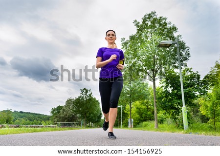 Urban sports - Woman running for better fitness in the city park on a cloudy summer day