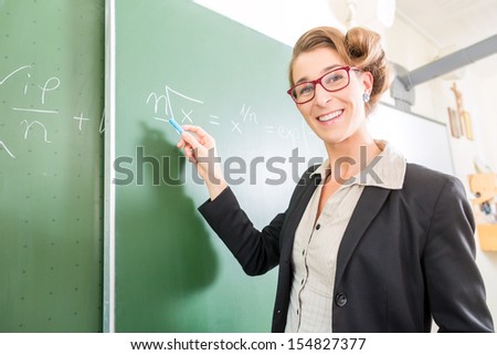 Teacher or docent writing with chalk on the board or  chalkboard or blackboard while math lesson in school class
