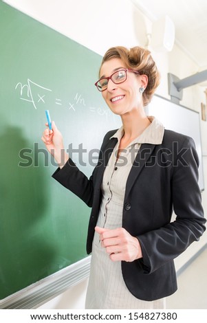 Teacher or docent writing with chalk on the board or  chalkboard or blackboard while math lesson in school class