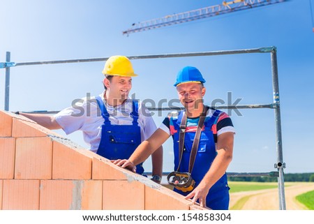 Two proud construction site workers or bricklayers standing on house project directing the crane with a remote control