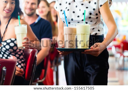 Friends or couples eating fast food and drinking milk shakes on bar in American fast food diner, the waitress is taking orders