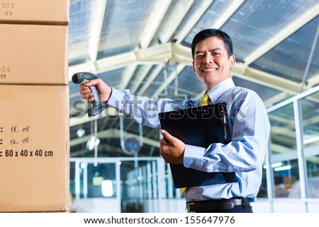 Young Indonesian man in a suit with a bar code scanner in a Asian warehouse