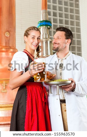 Young man and woman in traditonal Tracht with beer glass in brewery, in front of brewing kettle