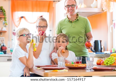 Family, father and children or daughter with friends in the kitchen at the table eating healthy fruits