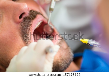 Male patient with dentist and assistant in a dental treatment, wearing masks and gloves, giving anesthetization syringe
