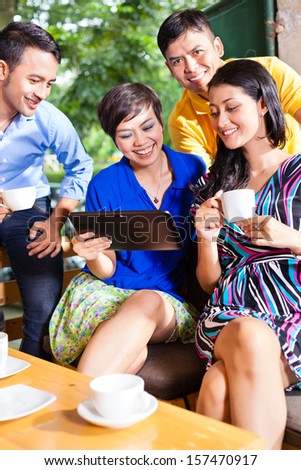 Asian friends or colleagues enjoying leisure time in a cafe, drinking coffee or cappuccino and looking at photos or emails on a tablet computer