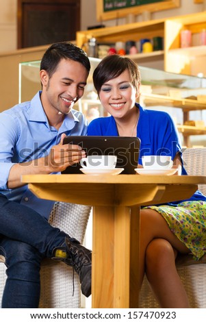 Asian friends enjoying her leisure time in a cafe, drinking coffee or cappuccino and looking at photos or emails on a tablet computer