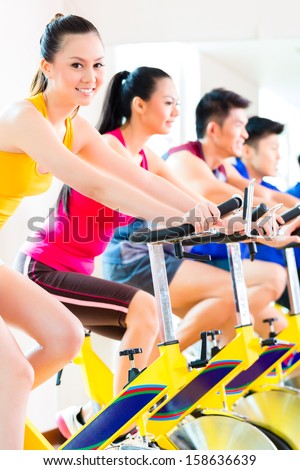 Chinese Asian sport group of men and women in fitness club or gym exercising on bikes