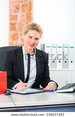 Young female lawyer working in her office with a typical law book and writing in a document