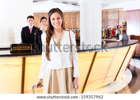 Asian Chinese woman arriving at front desk of luxury hotel in business clothes with trolley