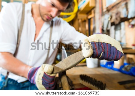 Young man in the Bavarian mountains grinds his axe and sharpening tools with a grindstone to chop the fire wood