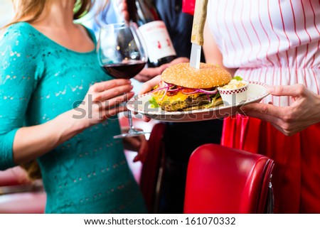 Friends or couple eating fast food in American fast food diner, the waitress serving the food, burgers, fries, and red wine