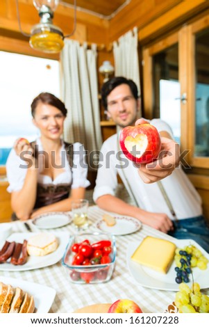 Couple in a traditional mountain hut having a meal, breakfasting with fruits, cold cuts, cheese and bread