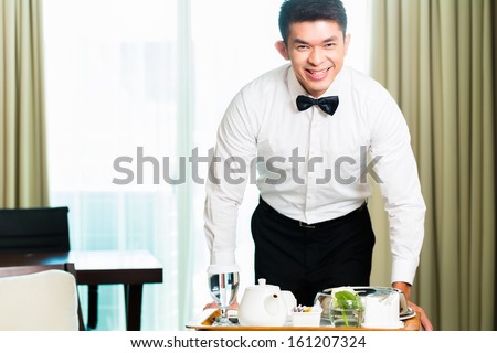 Asian Chinese room service waiter or steward serving guests food in a grand or luxury hotel room