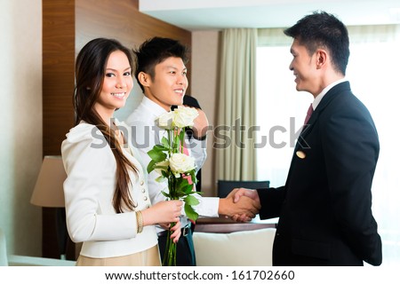 Asian Chinese Hotel Manager or director or supervisor welcome arriving VIP guests with roses on arrival in luxury or grand hotel