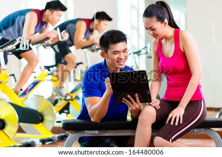 Asian Chinese Woman and personal fitness trainer in gym discussing training schedule and goals for workout