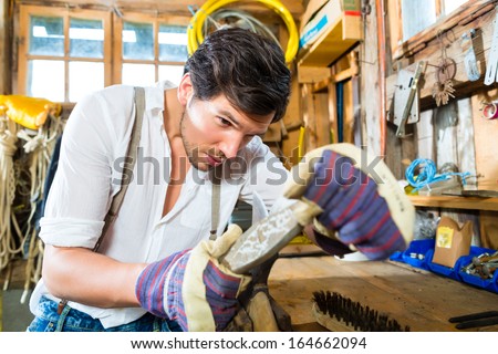 Young man in the Bavarian mountains grinds his axe and sharpening tools with a grindstone to chop the fire wood