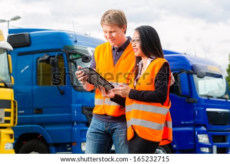Logistics - Proud Driver Or Forwarder And Female Coworker With Tablet Computer, In Front Of Trucks And Trailers, On A Transshipment Point, Its A Good And Successful Team