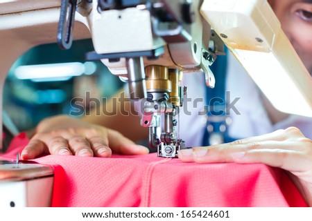 Asian Seamstress or worker in an Asian textile factory sewing with a industrial sewing machine, she is very accurate