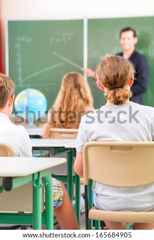 Teacher or educator or docent standing while lesson  in front of a blackboard and educate or teach students or pupils or mates in a school or class