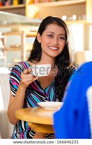Asian female friends enjoying her leisure time in a cafe, drinking coffee or cappuccino and talking about some things