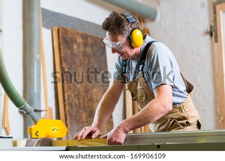 Carpenter working on an electric buzz saw cutting some boards, he is wearing safety glasses and hearing protection for workplace safety