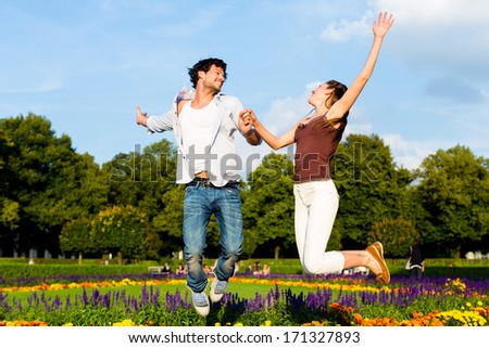 Man and woman or young couple making a trip as tourists in park jumping in the sun