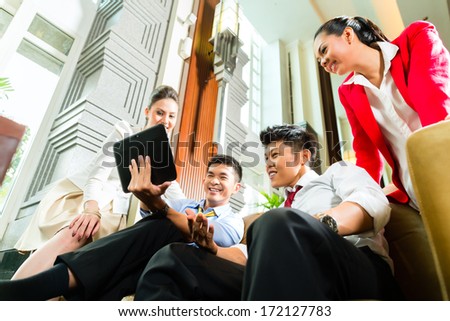 Group of four Asian Chinese businesspeople meeting for small team discussion in luxurious hotel lobby, there are documents on a tablet computer